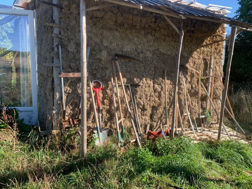 Garden tools resting against clay straw wall of greenhouse